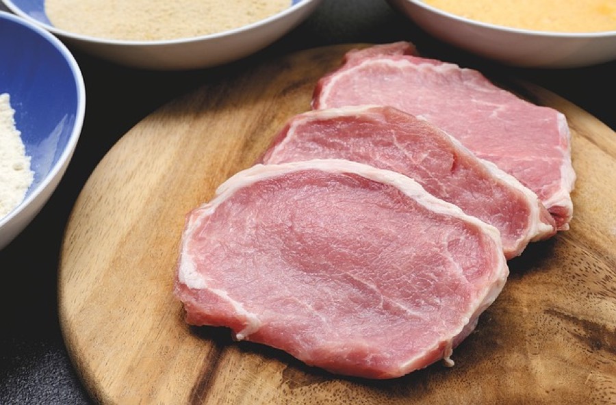 Three raw pork loin chops on a wooden board