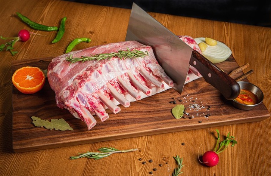 Raw rack of lamb with the fat cap on, resting on a wooden cutting board