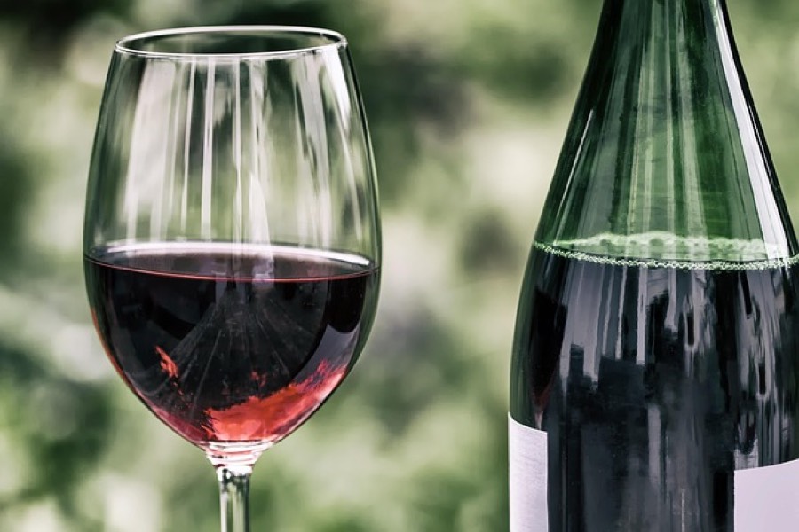 A glass of red wine next to an open bottle on a table outdoors