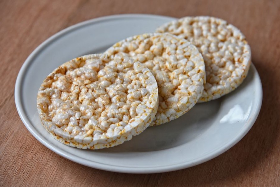 Three plain puffed rice cakes on a white plate on a wooden table