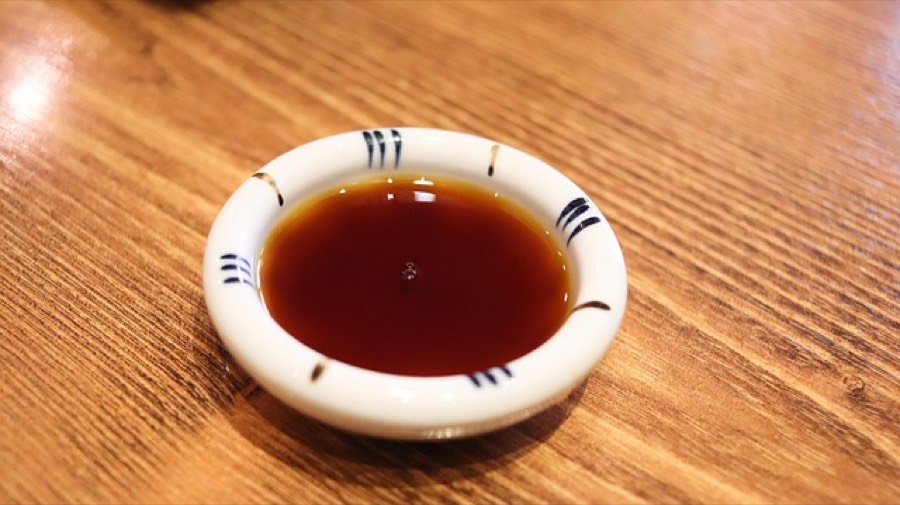 A small ceramic dish of dark soy sauce on a wooden table