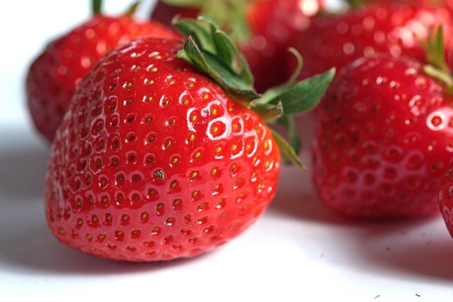 Fresh whole strawberries with green stems on a white surface