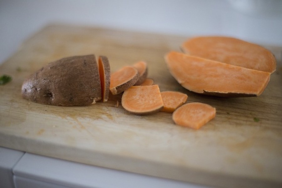 Raw sweet potato sliced on a wooden board, showing the orange flesh
