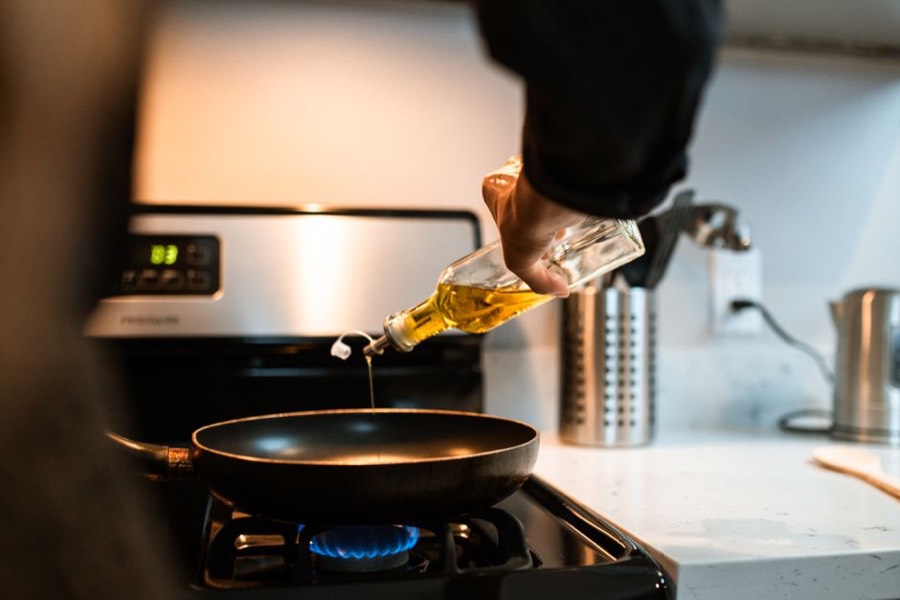 Pale golden vegetable oil being poured from a glass bottle into a frying pan on a gas hob