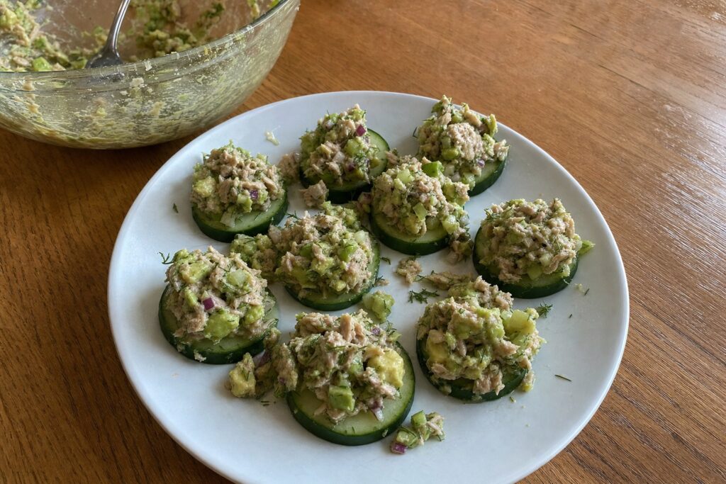 Cucumber rounds topped with avocado tuna salad on a plate, with the mixing bowl behind it