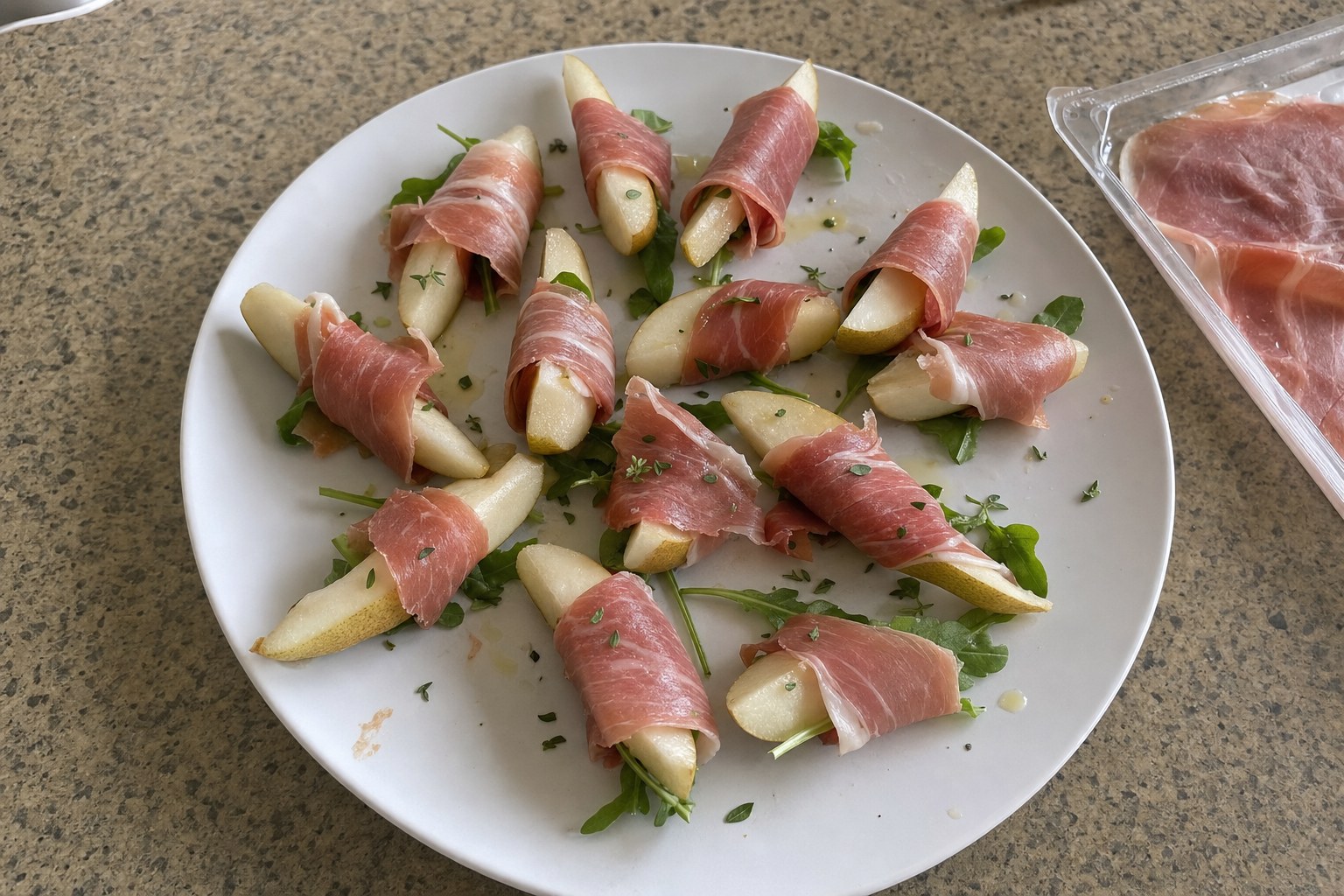 Pear wedges wrapped in prosciutto with arugula and thyme on a white plate